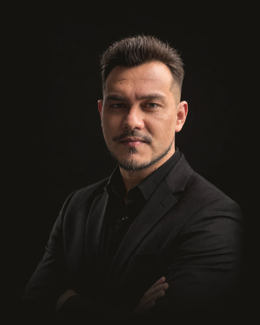 Theo Cristo, advogado, de terno e camisa pretos, fotografado em estúdio com fundo escuro